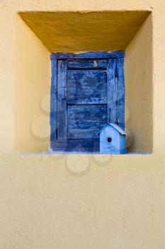 Blue painted shutter closing window in thick stone wall of house with small birdhouse on shelf