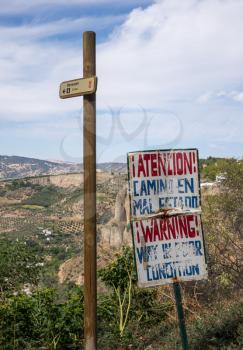 Sign advising danger of poor condition footpath down into valley over the cliff face at Ronda, Andalucia, Spain