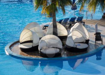 Circular relaxing beds and loungers with shades by side of hotel swimming pool