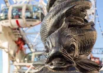 Close up of a carved fish on railing by River Thames with London Eye out of focus in background. London, England