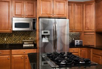 View over island gas hob to refrigerator and microwave oven in cherry cabinet modern luxury fitted kitchen