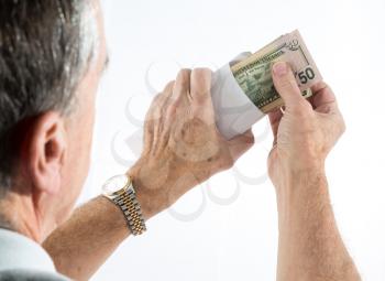 Stack of fifty and twenty US dollar bills being put in envelope by senior caucasian hands with side view of head as though looking over shoulder