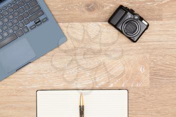 Tidy organized desk top with laptop, camera and notebook with pen on an oak wooden table for designer workspace
