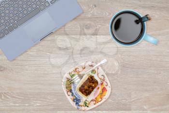 Tidy organized desk top with laptop, cup of coffee and fruitcake on an oak wooden table for designer workspace