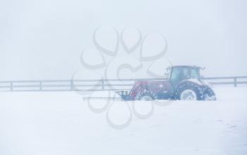 Tractor fitted with plow attachment clears a local road in snow blizzard conditions