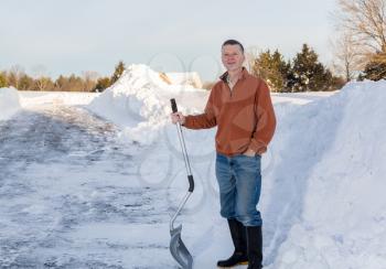 Senior man with snow shovel looking content after removing snow drifts on driveway by digging out from the blizzard