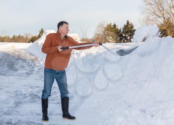 Senior man with snow shovel finishes removing snow drifts on driveway by digging out from the blizzard