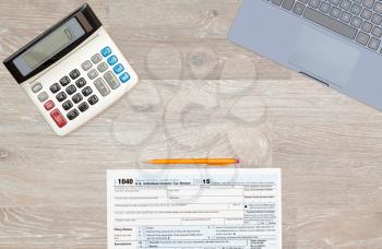 USA IRS tax form 1040 for year 2015 with pencils and calculator with a laptop keyboard on wooden desk and taken from above