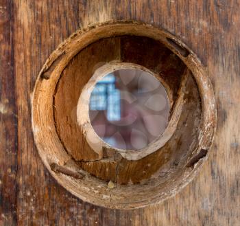 Ghostly face looking through a wooden door with small peep hole or viewing lens in the doorway