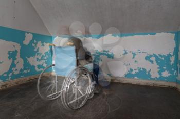 Ghostly person in old wheelchair in motion blur and trapped in corner of a room