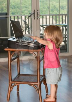Young two year old girl typing with finger on laptop touchscreen on wooden table