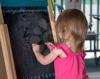 Young two year old girl drawing with chalk on blackboard and using both hands ambidextrously