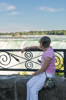 Senior woman looks at Canadian or Horseshoe waterfall from Canadian side of Niagara Falls