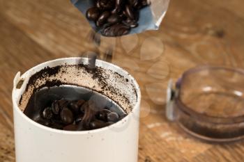 Macro view of coffee beans being poured into electric grinder standing on old wooden kitchen table