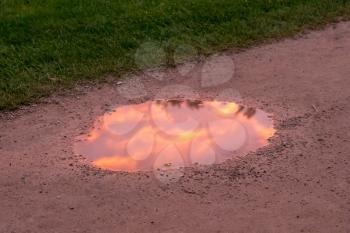 Bright reflection of sunset clouds and sky in a muddy puddle in a gravel track or path