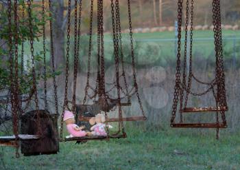 Halloween image of an abandoned childs dolly and small soft toy of girl on old rusty swing at fun fair