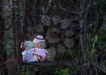 Halloween image of an abandoned childs dolly and small soft toy of girl on old rusty swing at fun fair