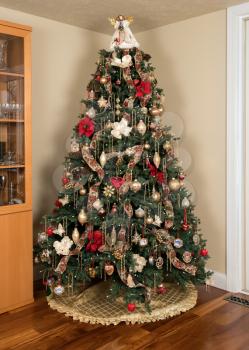 Ornately decorated christmas tree in the corner of a modern living room with cover under the branches