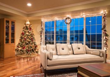 Ornate and decorated Christmas Tree in the corner of living room of modern family home as night falls outside the apartment