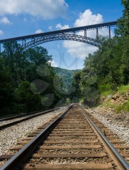 Railway rails alongside river underneath the high arched New River Gorge bridge in West Virginia