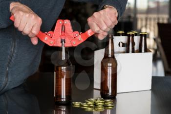 Brewer of home brewed beer using a red bottle capper to attach the metal cap to the top of the glass bottle with a six pack in background.