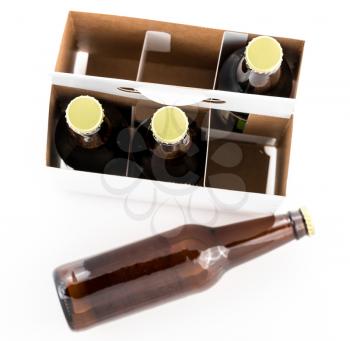 Pattern of three beer bottles in six pack cardboard container with gold caps facing upwards, with a fourth bottle laying on the table top