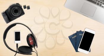 Clean and tidy wooden desk with equipment ready for travel including camera, laptop, phone, music player and passports