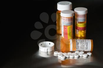 Oxycodone is the generic name for a range of opoid pain killing tablets. Prescription bottle for Oxycodone tablets and pills on metal table for opioid epidemic illustration