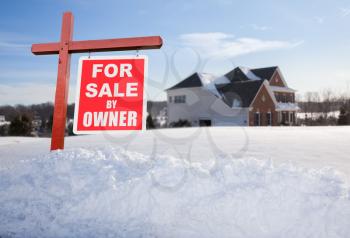 For Sale by owner real estate sign in front of large brick single family house in expansive snow covered yard in mid winter