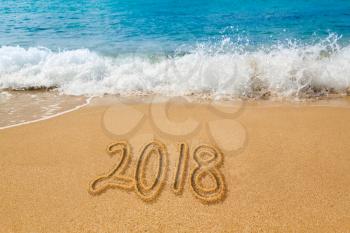 Sand drawing on warm beach by ocean surf in Caribbean spelling 2018 as an illustration of Happy New Year