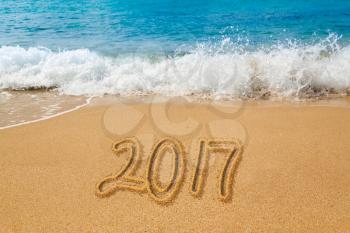 Sand drawing on warm beach by ocean surf in Caribbean spelling 2017 as an illustration of Happy New Year