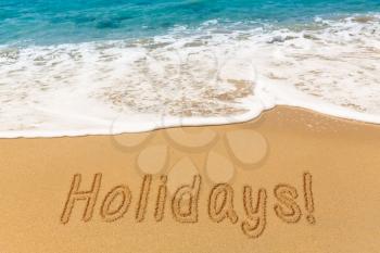 Holidays word written into sand on beach by warm blue ocean in Caribbean advertising vacations and holidays