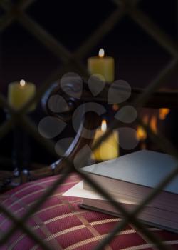 View from outside old window at an abandoned book with marker on a carved chair with firelight and candles in background to give a warm cozy winter feeling