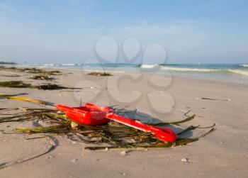 Lost or abandoned red childs spade on sandy beach with ocean in distance to give concept of loss or danger
