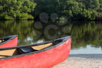Two red prows of canoes or kayaks with an open pond or river beach in background ready for paddling expedition