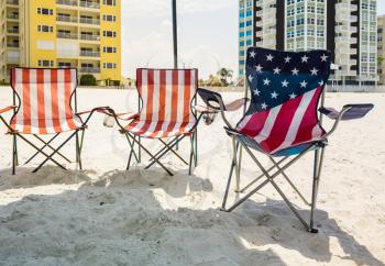 Three folding chairs on sandy beach in the design of US flag of stars and stripes