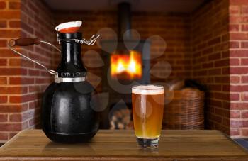 Large 64 fluid ounce four pint growler bottle with a glass of cold beer or ale in front of fire. Used by microbreweries to serve beer for home consumption