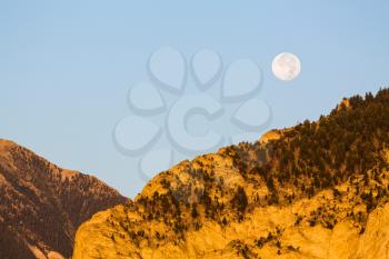 Valley by chalk white cliffs of Mount Princeton near Buena Vista in Colorado as setting moon drops over horizon at sunrise