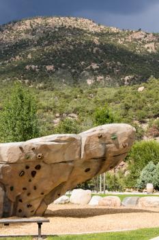 Climbing wall with hand holds and bolted fasteners with real mountain and rocks in the background