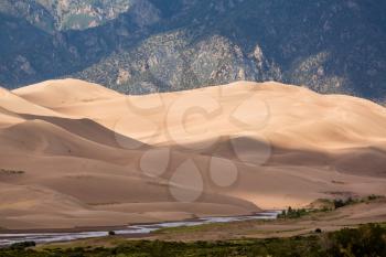 Closer detail of the dunes at Great Sand Dunes National Park in Colorado with the mountains behind. The river from the mountains flows by the sand