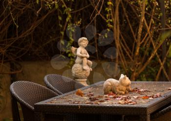 Warm colors of rustic autumn garden table with falling leaves and statue of cat and angel in background