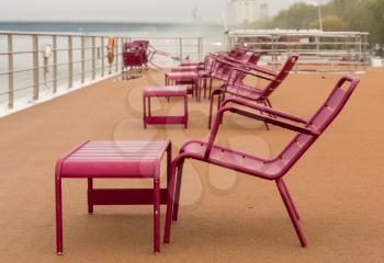 Purple or red chairs and table on deck of river cruise boat in mist and rain