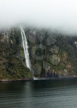 Waterfall on side of Milford Sound on South Island of New Zealand in early morning as the sun rises above the mountains