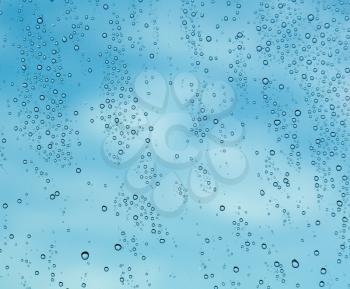 Blue color of sky and clouds behind rain or spray drops on window of cruise ship as the sun starts to rise at dawn and illuminate the water