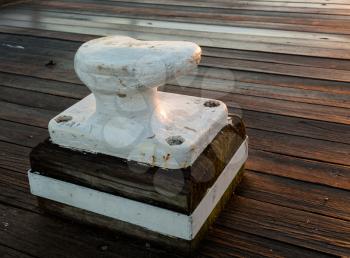 Setting sun shines warm light on a white painted ships bollard for securing a boat. Mounted on old wooden pier or decking
