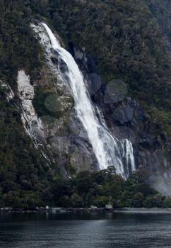 Waterfall on side of Milford Sound on South Island of New Zealand in early morning as the sun rises above the mountains
