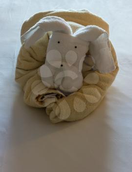 Unusual animal shaped like a dog or teddy bear created from rolled and folded towels on top of bed sheets in hotel