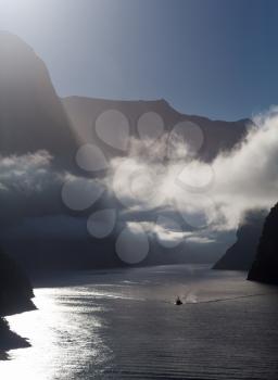 Sailing into Milford Sound on South Island of New Zealand in early morning as the sun rises above the mountains