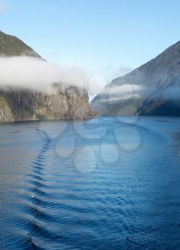 Sailing into Milford Sound on South Island of New Zealand in early morning as the sun rises above the mountains