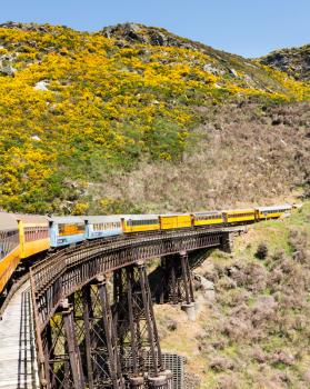 Train and coaches of Taieri Gorge tourist railway run sacross a steel trestle bridge over a ravine on its journey up the valley